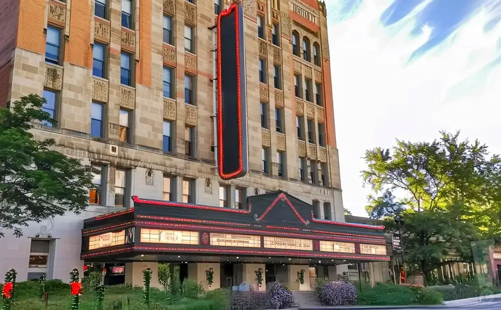 Marquee lights up a historic brick and stone theater building with trees in the foreground.