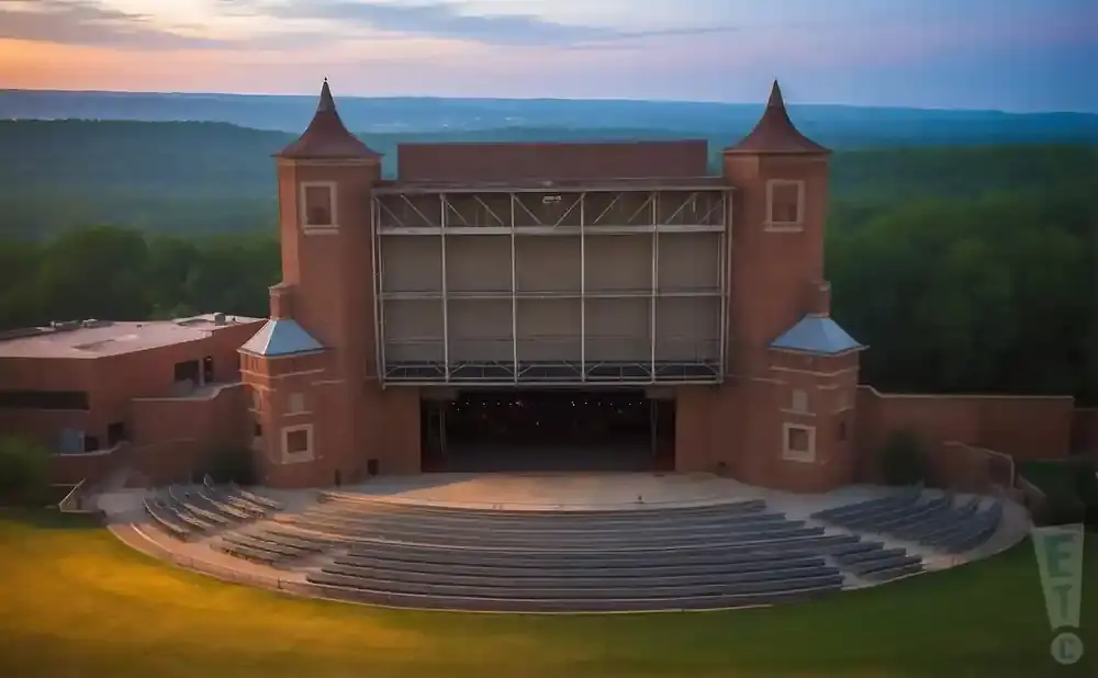 An outdoor amphitheater at sunset with a brick building, stage, and tiered seating.