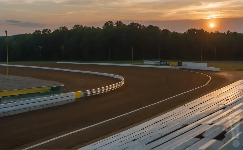 Dirt racetrack at sunset with trees and a fence lining the track.