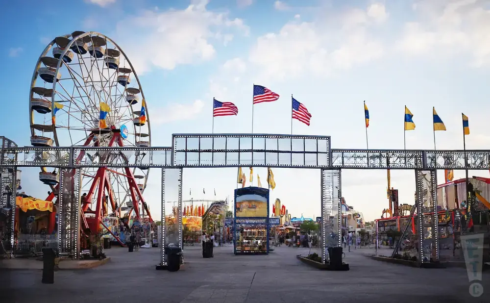 A Ferris wheel and carnival rides under a cloudy sky with American flags.