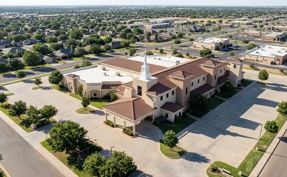 Aerial view of a church building with a steeple, surrounded by a parking lot and a suburban neighborhood.