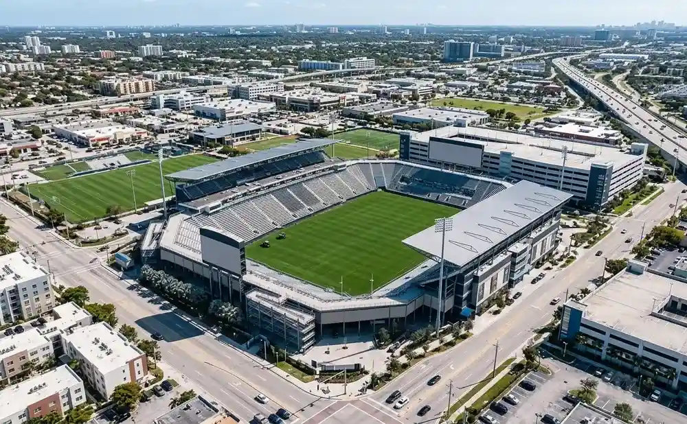 Aerial view of a modern soccer stadium with a green field, surrounded by urban development and a highway.