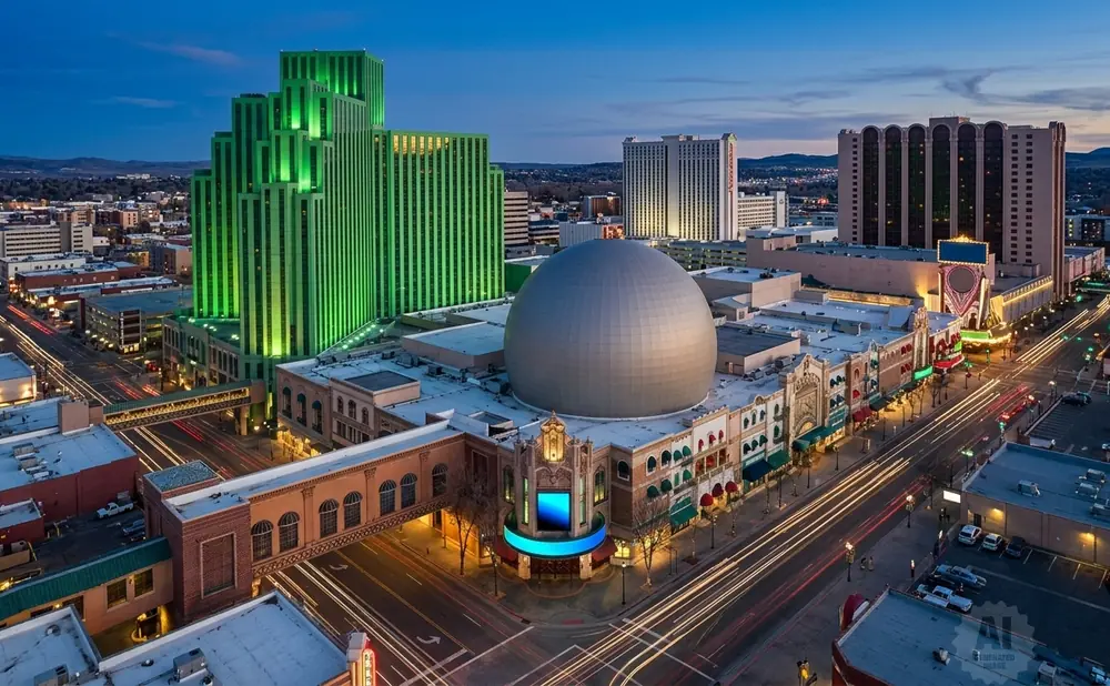 Aerial view of a city skyline at dusk, featuring a prominent green skyscraper and a large domed building.