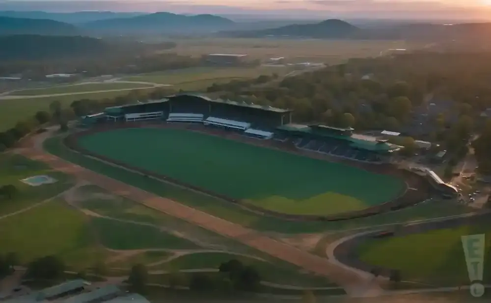 Aerial view of a racetrack with green infield and grandstands, at sunset.