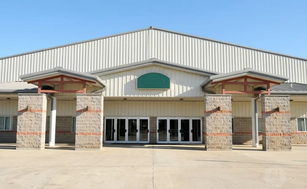 Large, light-colored metal building with a central entrance featuring double glass doors flanked by brick columns.