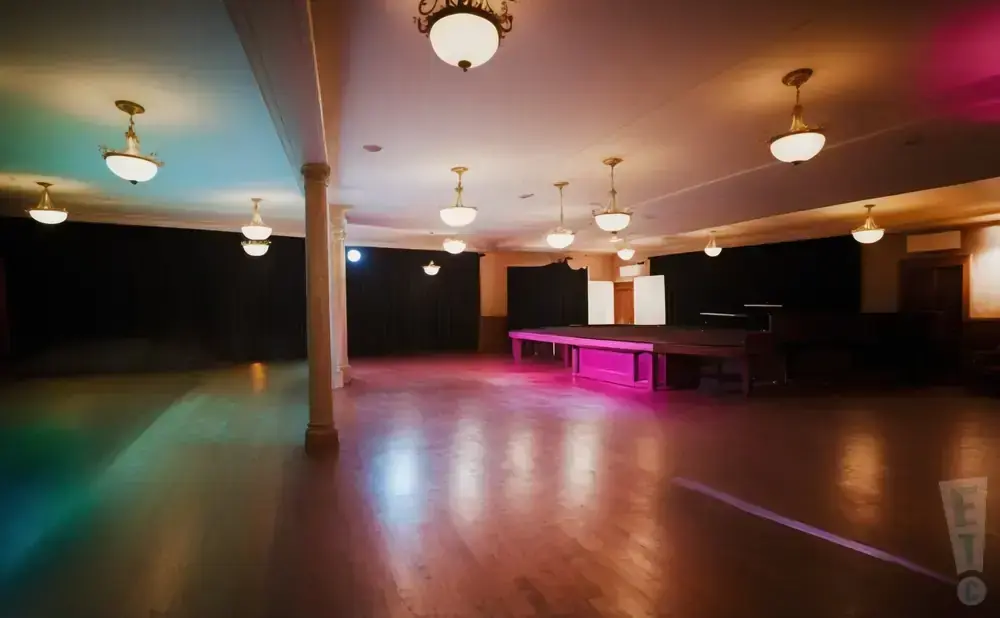 A large, empty ballroom with a wooden floor, chandeliers, and stage lighting.