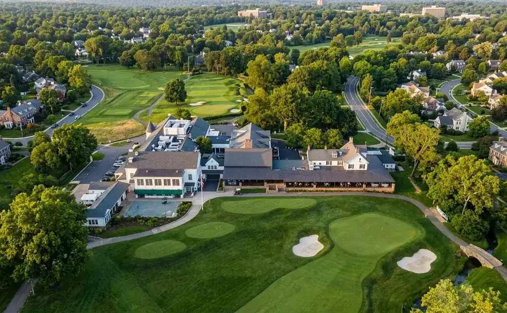 Aerial view of a golf course and clubhouse surrounded by trees and residential homes.