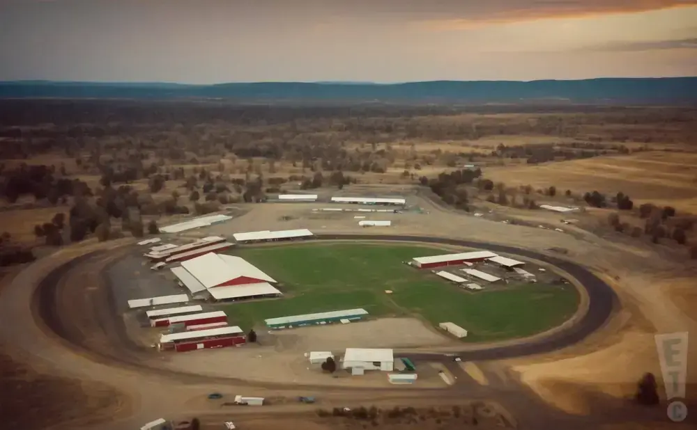 Aerial view of a rural race track with agricultural buildings and surrounding fields at dusk.