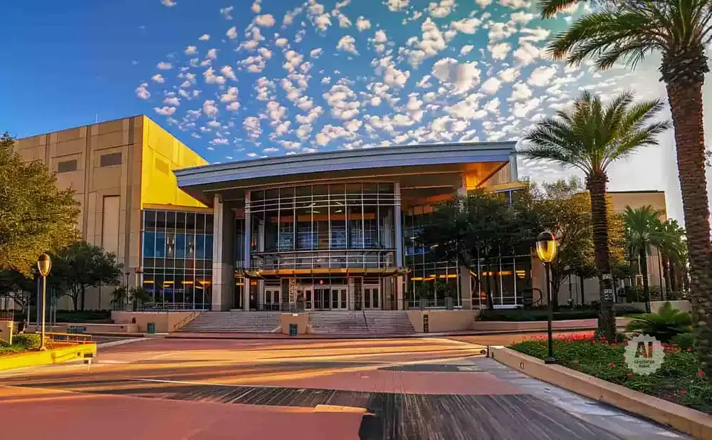 Modern building with large glass entrance, palm trees, and a bright, cloudy sky.