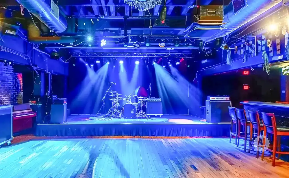 A dimly lit bar stage with a drum set and piano under blue spotlights.