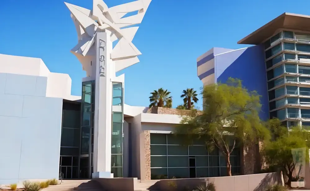 Modern building with abstract sculpture and palm trees under a clear blue sky.