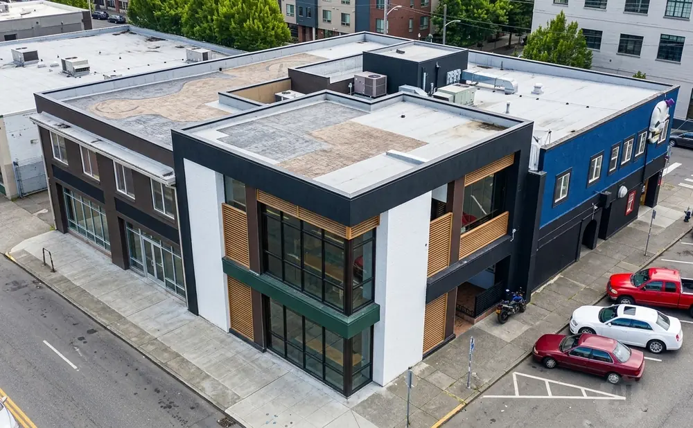 Aerial view of a blue and black building with large windows, parked cars, and a red pickup truck.