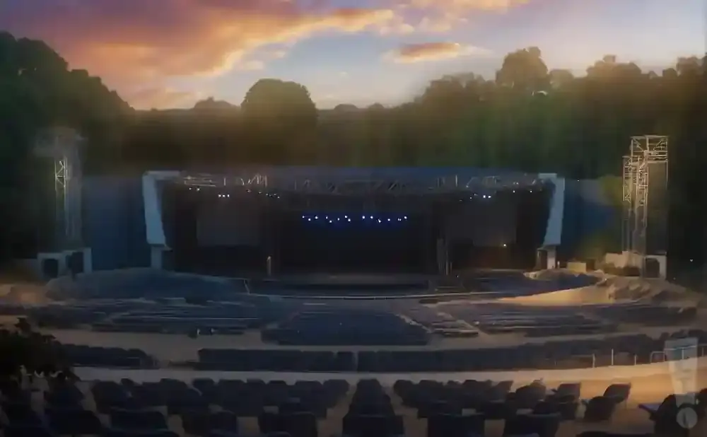 Outdoor amphitheater stage with seating areas under a sunset sky.