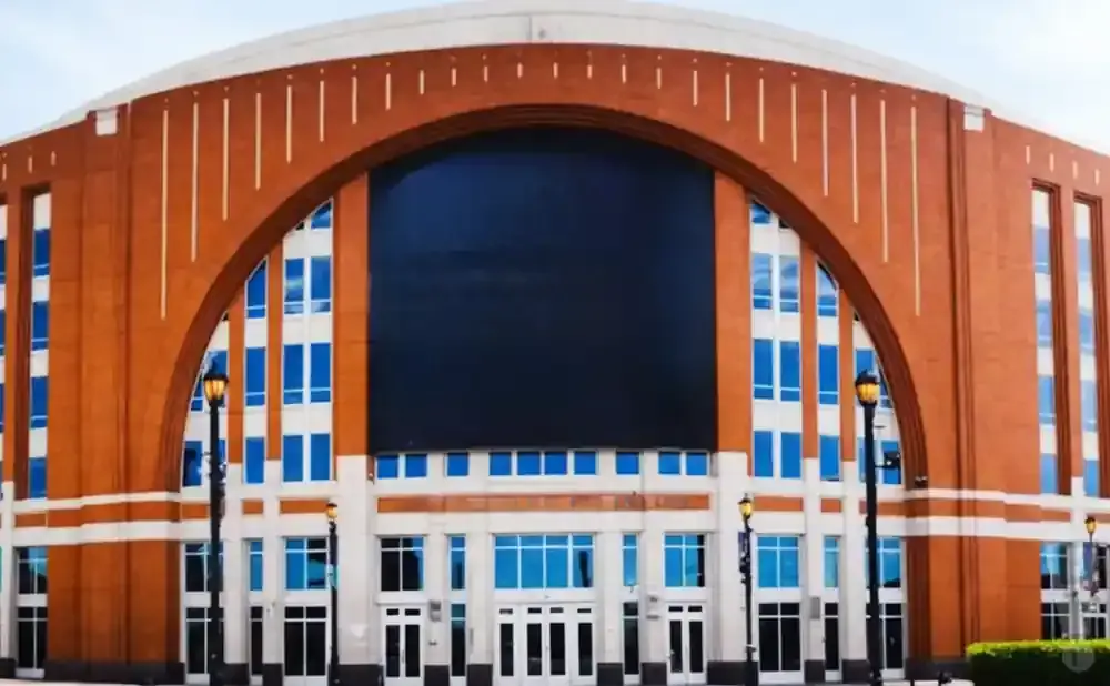 Large brick arena with a giant dark screen under an arch, blue windows, and ornate lampposts.
