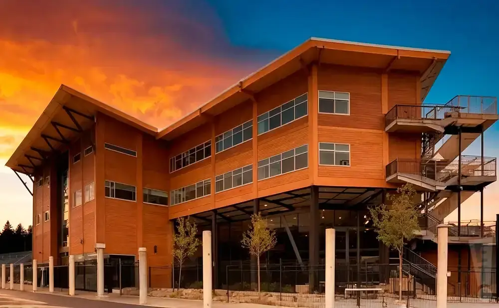 Modern wooden building with large windows and an exterior staircase against a vibrant sunset sky.