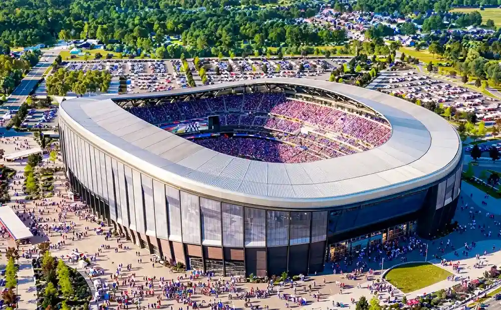Aerial view of a packed stadium with a curved roof and surrounding parking lots and trees.