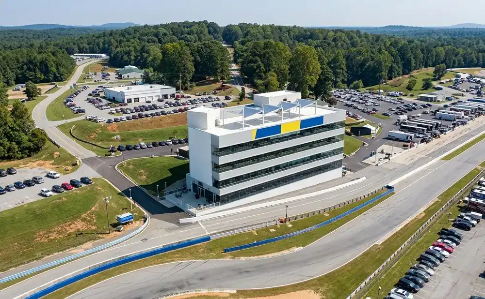 Aerial view of a modern multi-story building at a race track, with parked cars and RVs.