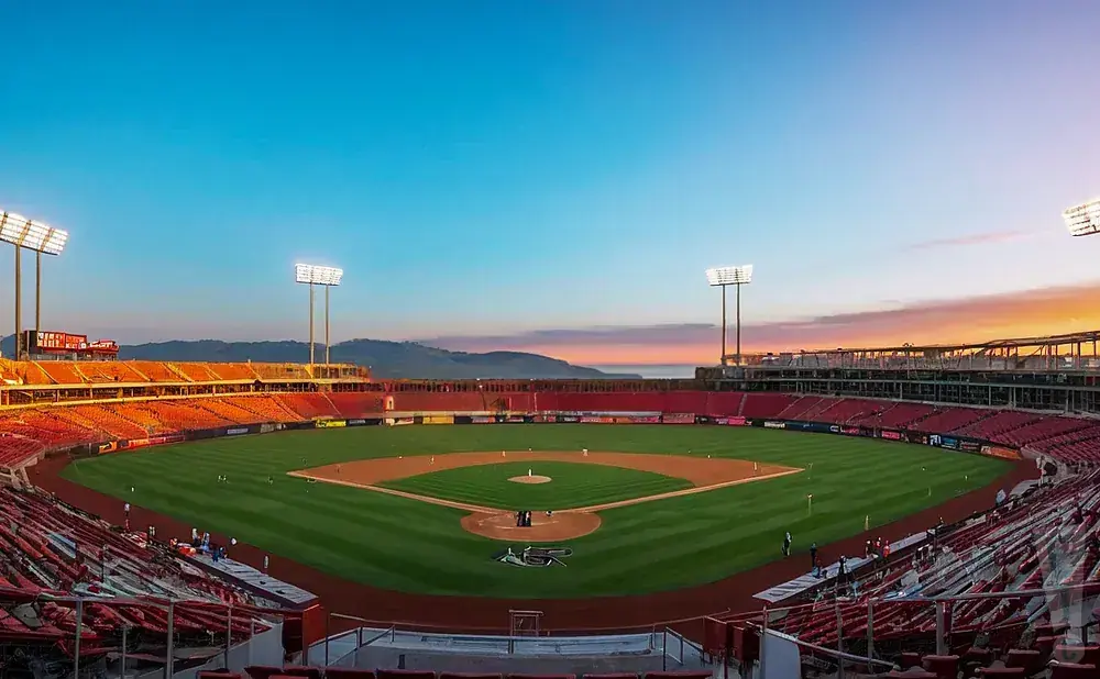 A baseball stadium at sunset with red seats and a green field.