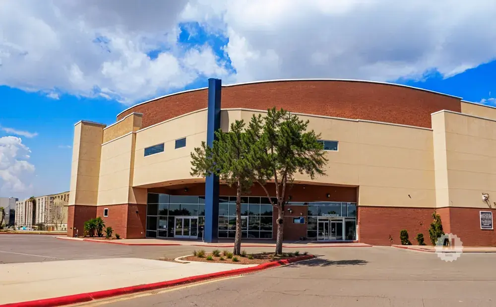 A large, modern building with a curved brick upper level and tan lower level.