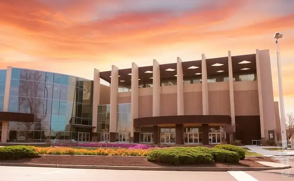 Modern building with glass facade and beige concrete pillars under a colorful sunset sky.