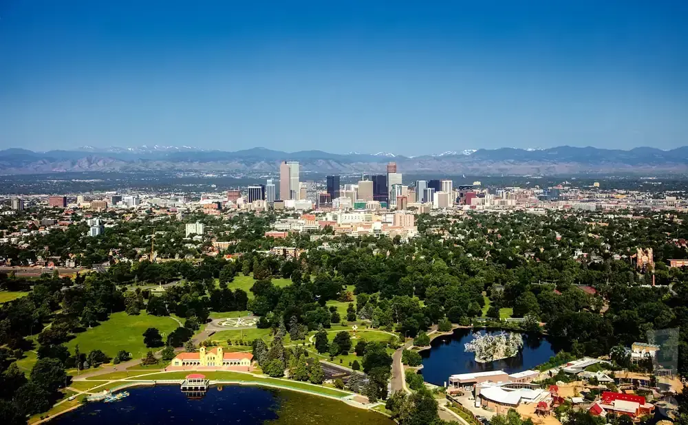 Aerial view of Denver, Colorado skyline with mountains in the background and a park with a lake in the foreground.