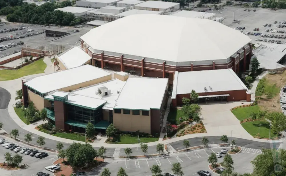 Aerial view of a large white domed arena with surrounding buildings and parking lots.