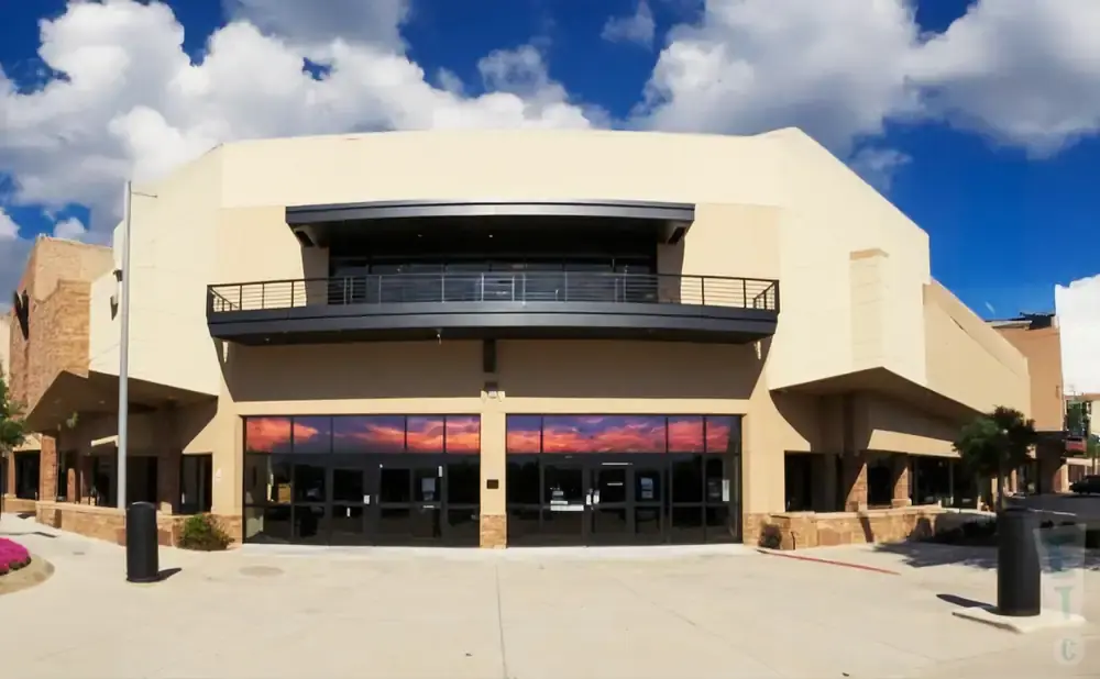 A modern building with a balcony and large glass doors reflecting a sunset sky.