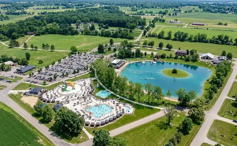 Aerial view of a water park with pools, slides, and a large lake surrounded by trees and parking lots.