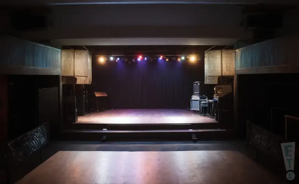 Empty stage with lighting rig, sound equipment, and audience seating area.