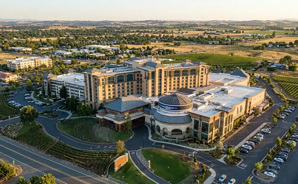 Aerial view of a large hotel and casino complex surrounded by vineyards and rolling hills.
