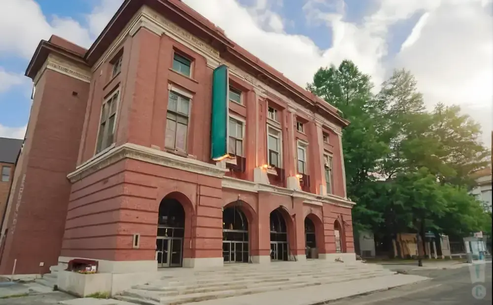Red brick building with arched entrances and large windows, a green banner hangs from the facade.