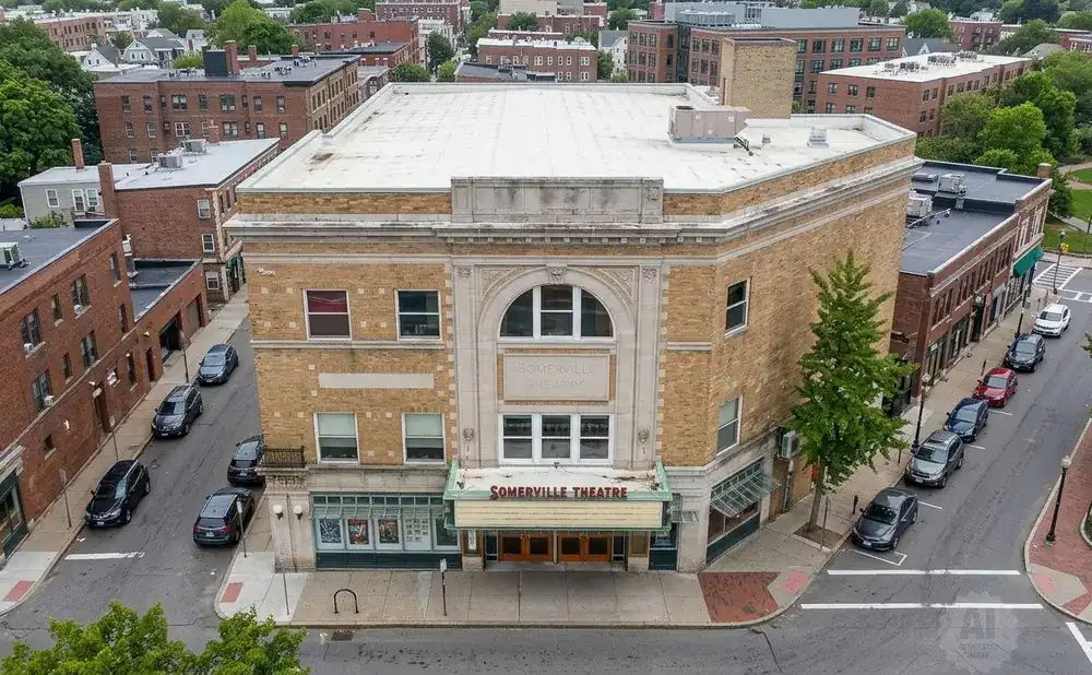 Aerial view of the Somerville Theatre, a yellow brick building with a marquee, surrounded by streets, sidewalks, and other brick buildings.
