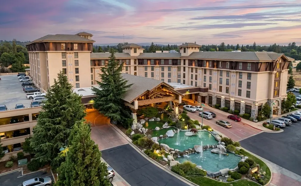 A large hotel with a rustic entrance, surrounded by trees and a pond.
