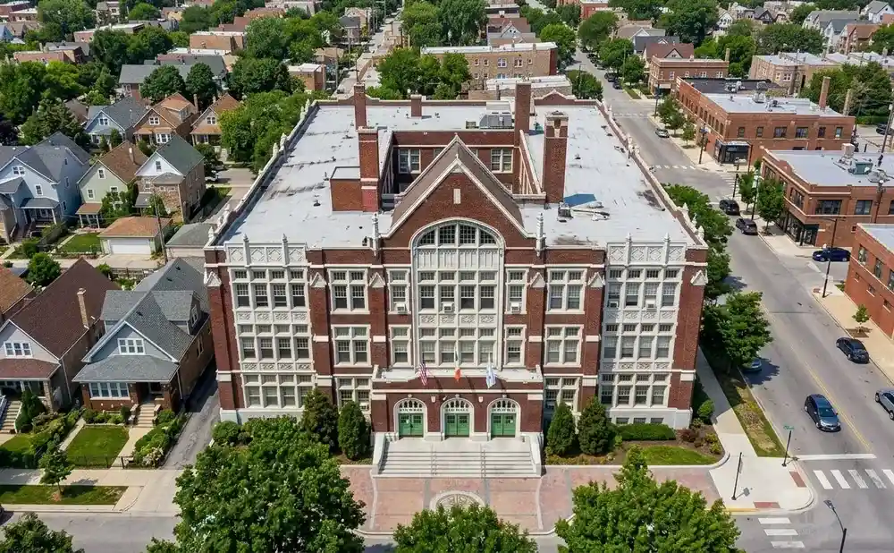 Aerial view of a large, brick school building with white trim, surrounded by trees and residential homes.