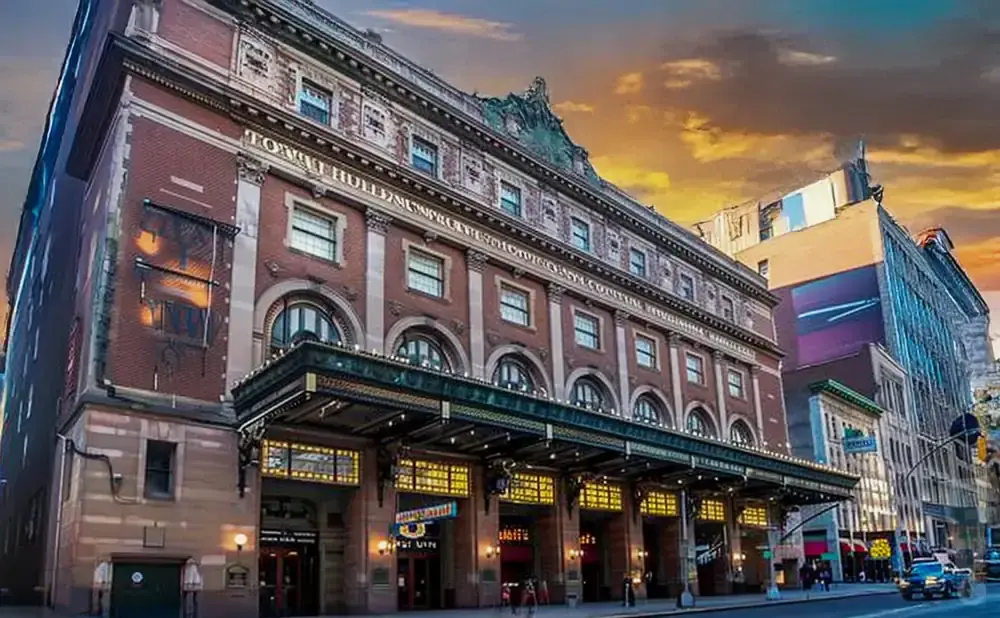 Town Hall theater in New York City with marquee lit up, at sunset.