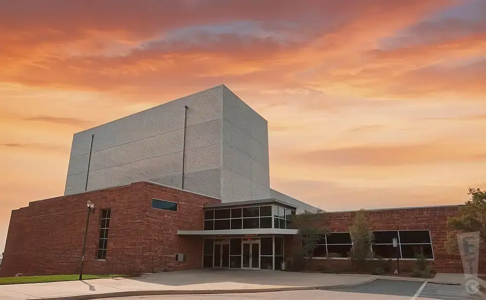 Modern brick building with a large silver facade against a dramatic orange and pink sunset sky.