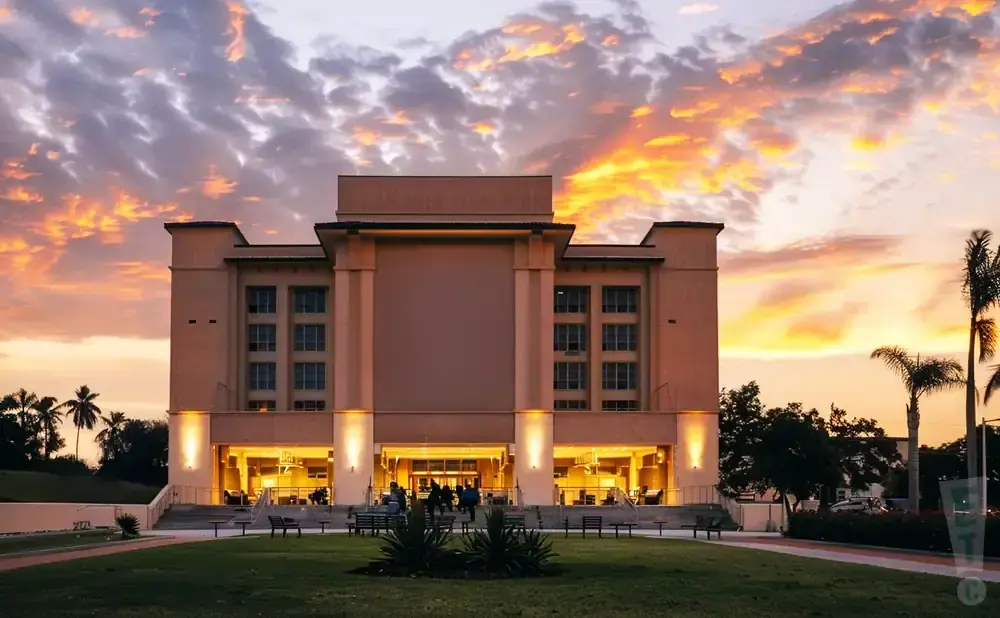A building with illuminated windows stands against a vibrant sunset sky with colorful clouds.