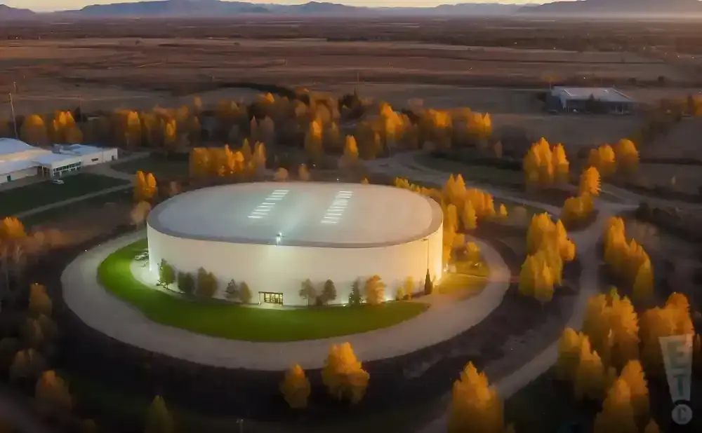 Aerial view of a large, round building surrounded by autumn trees during dusk.
