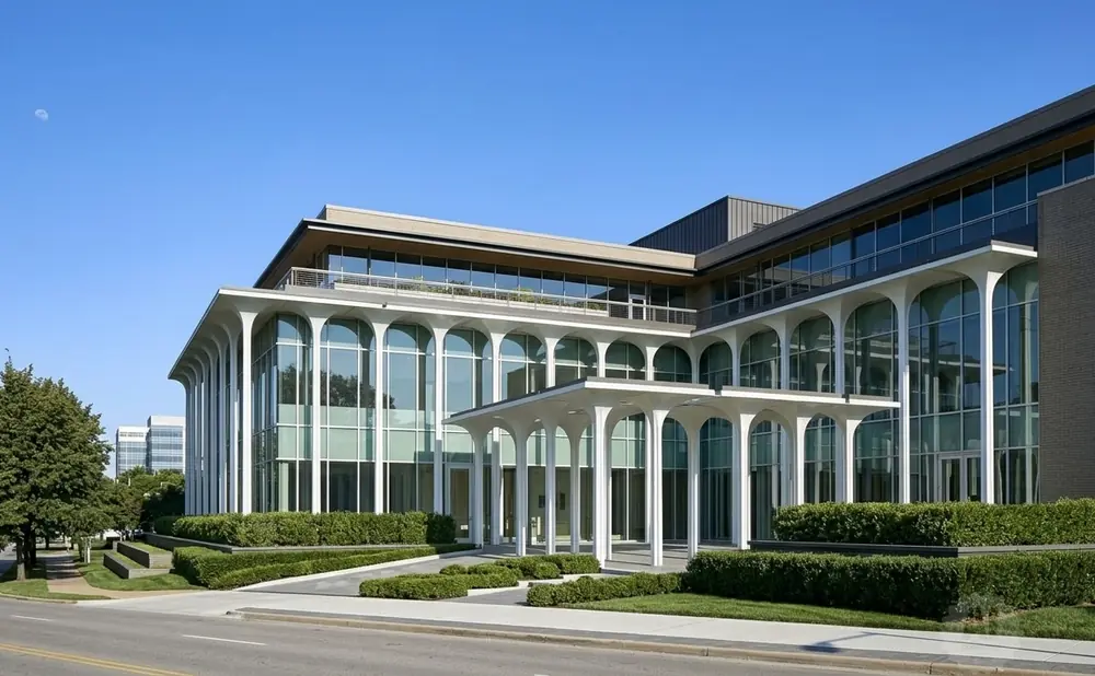 Modern office building with arched windows, a covered entrance, and manicured hedges.