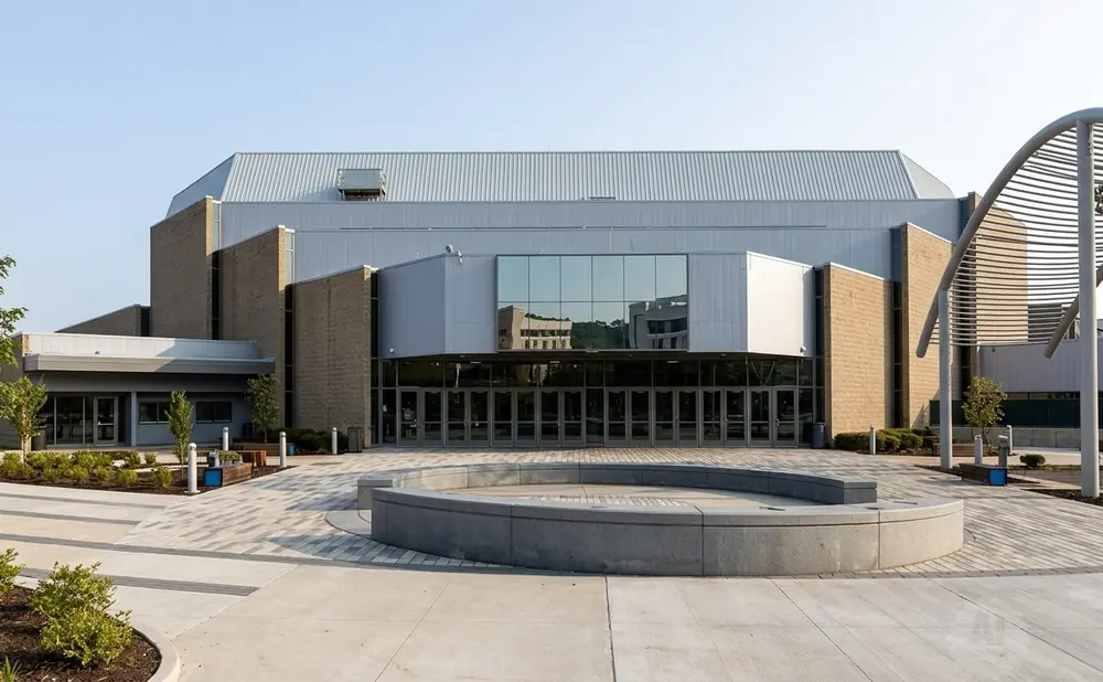 Modern building with large glass entrance and circular concrete seating area in a paved plaza.
