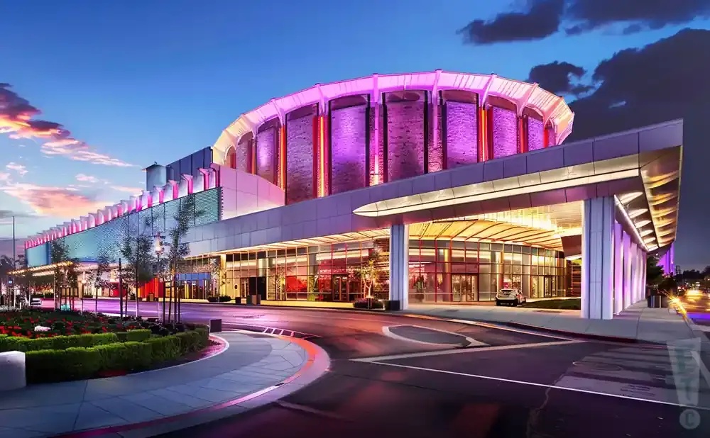 A modern casino at twilight, illuminated by purple and pink lights, with a circular dome and glass entrance.