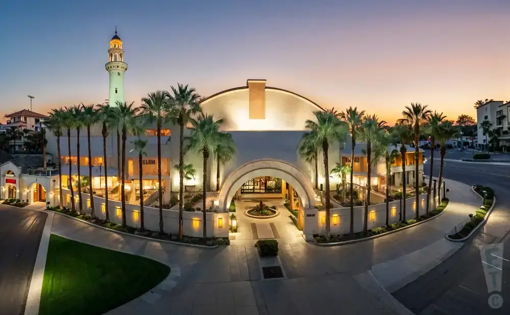 Elegant resort at dusk with palm trees, archway entrance, and a tall tower with a golden cap.