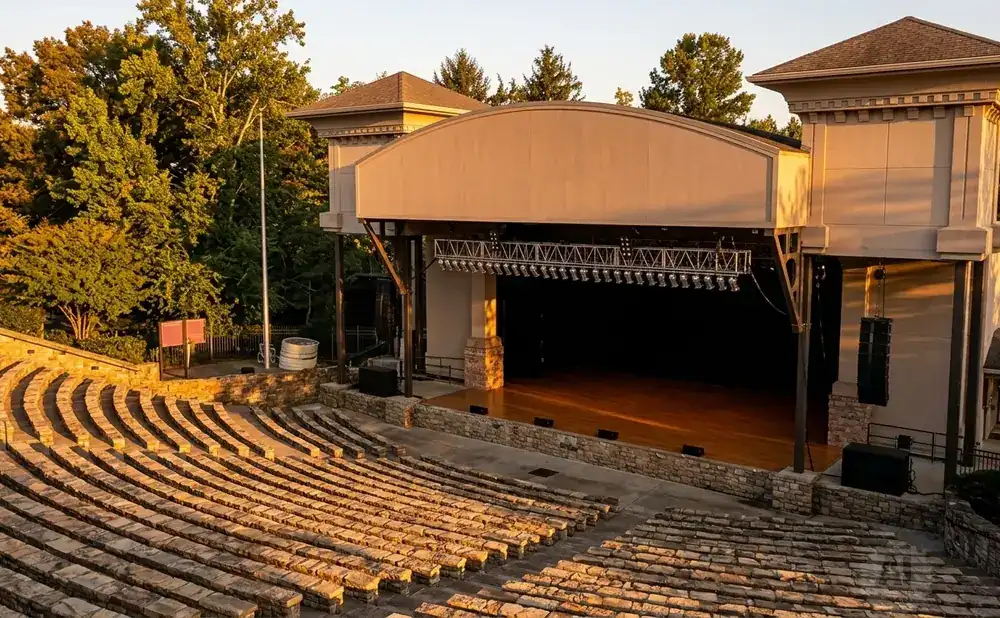 Outdoor amphitheater with stone seating and a stage under a covered pavilion, bathed in warm, golden sunlight.