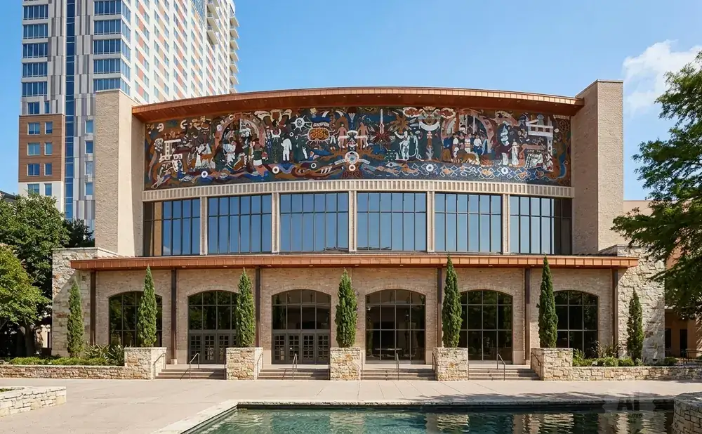 Building with a mosaic mural above large windows, flanked by trees and a pool.