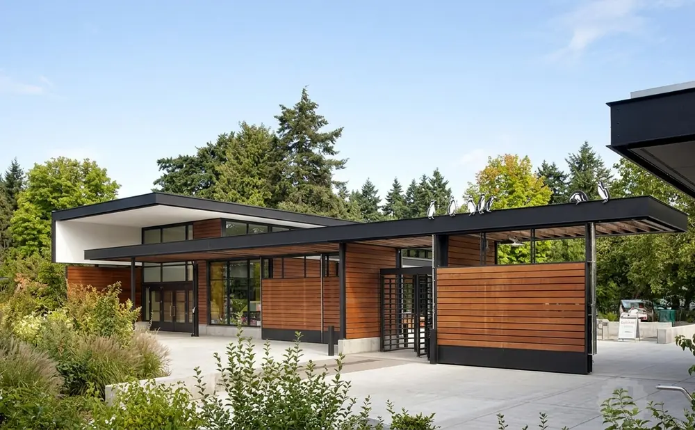 Modern wooden building with black roof, surrounded by trees, and penguins on the roof.