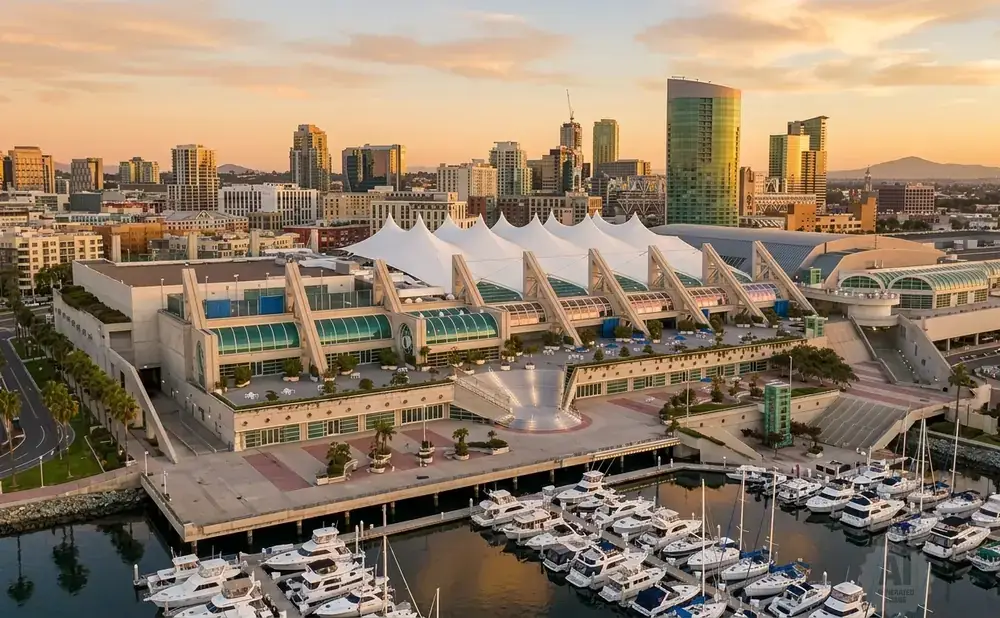 San Diego Convention Center with boats docked in the harbor and a city skyline at sunset.