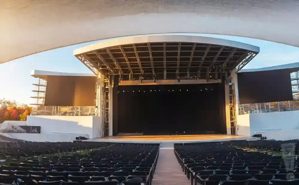 An outdoor amphitheater with rows of empty seats facing a large stage under a white canopy.