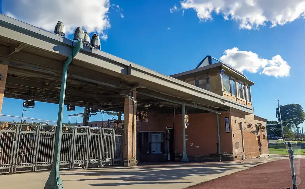 A brick building with a metal roof and gates under a bright blue sky with clouds.