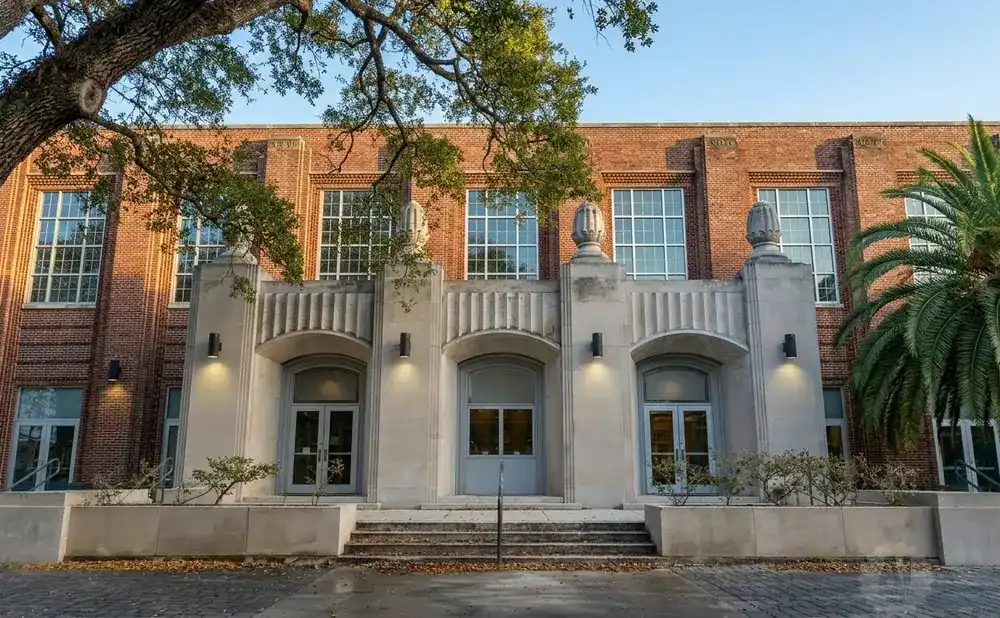 Brick building with large windows, stone facade, and palm trees.