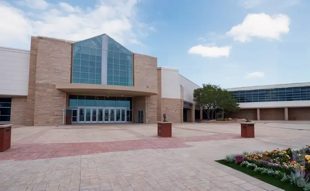 Exterior of a modern building with large glass windows and stone accents, a courtyard with planters and a sculpture.